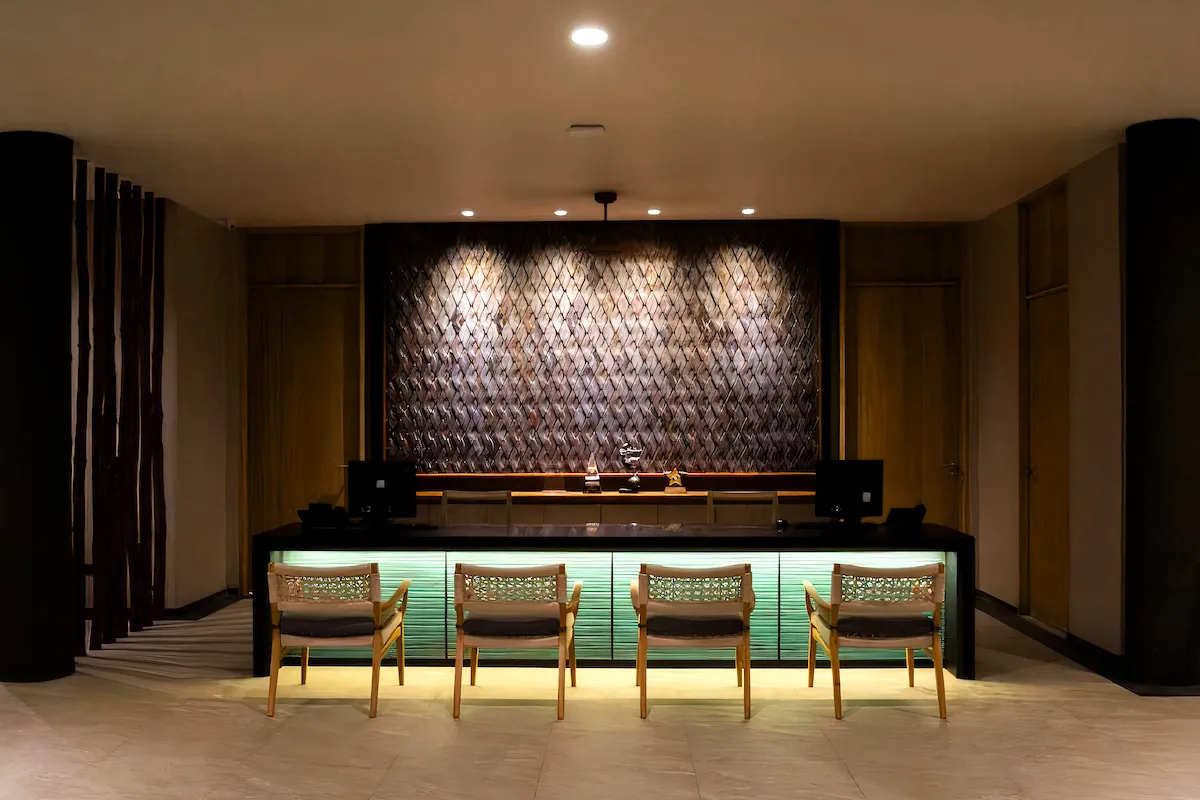 Elegant reception area at Andaman Cannacia Resort in Phuket, featuring a modern wooden front desk with woven chairs and a decorative textured wall backdrop